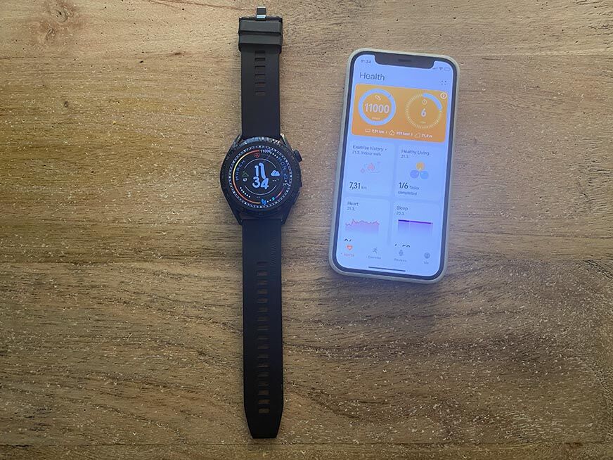 Man sieht die Huawei Watch GT 3 neben einem iPhone auf dem Tisch liegen. 